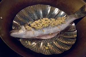 The fish, on the steamer tray, in the wok, over the boiling water